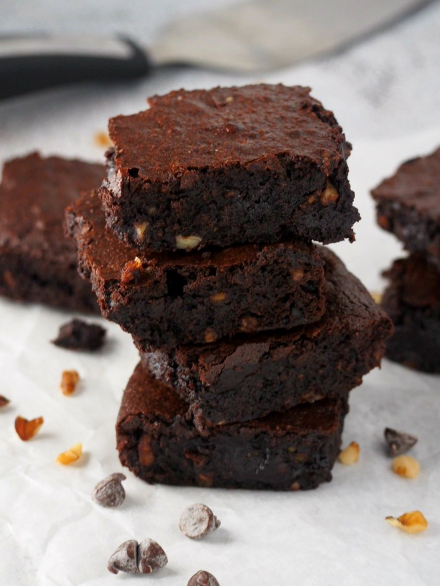 A stack of coconut oil brownies surrounded by chopped walnuts and chocolate chips.