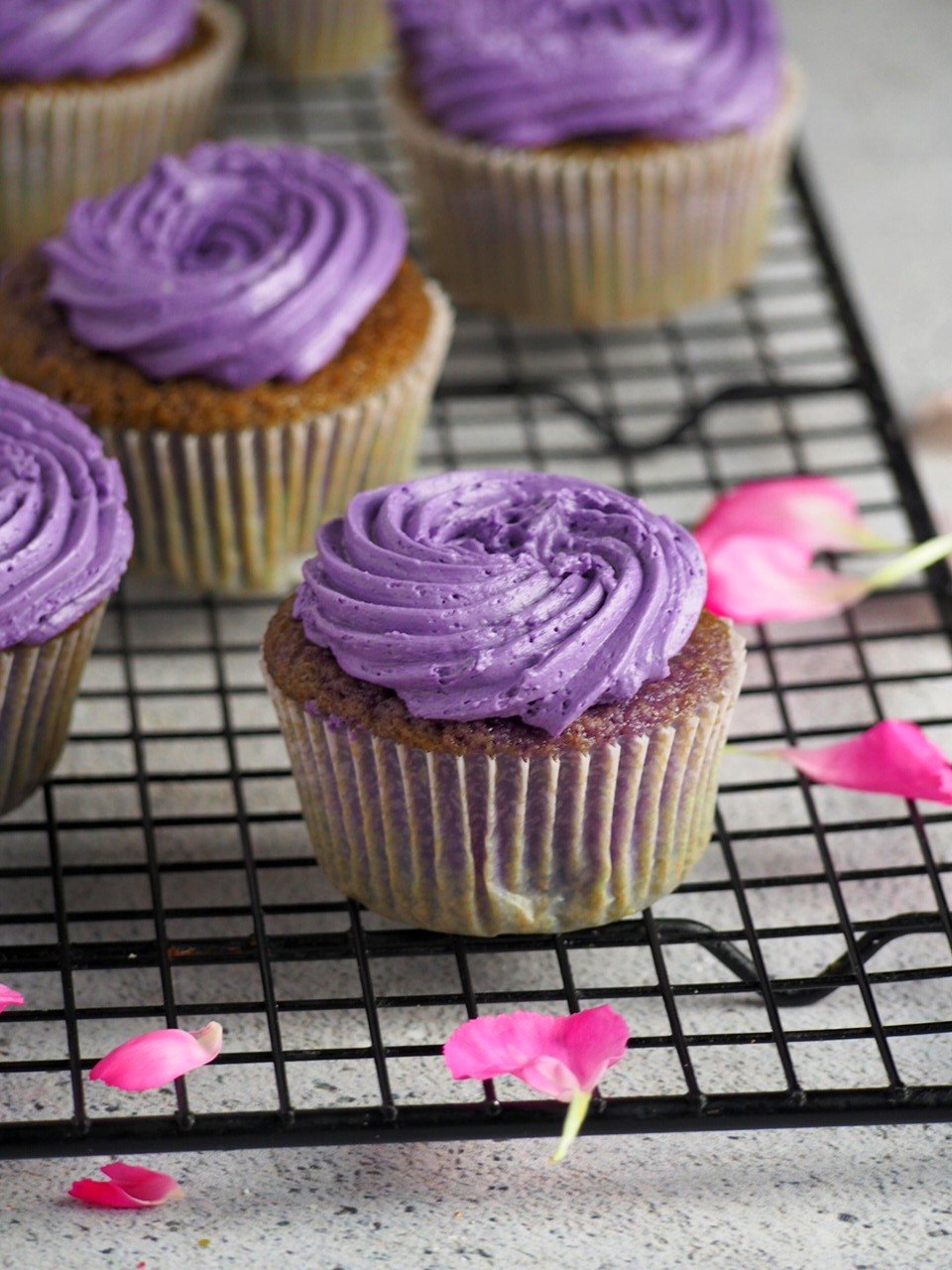Ube cupcakes lined on cooling rack and surrounded by flower petals.