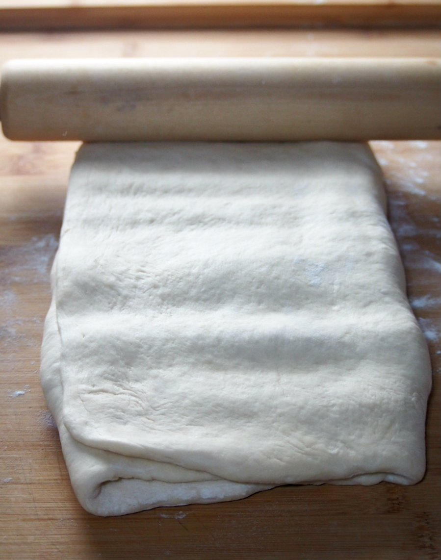 Making indentions on the dough surface using a rolling pin to soften the butter inside.
