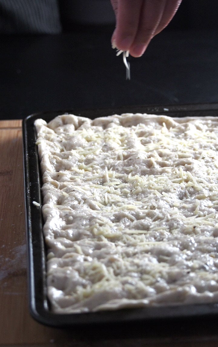 Parmesan cheese is being sprinkled on top of the focaccia bread dough prior to baking.