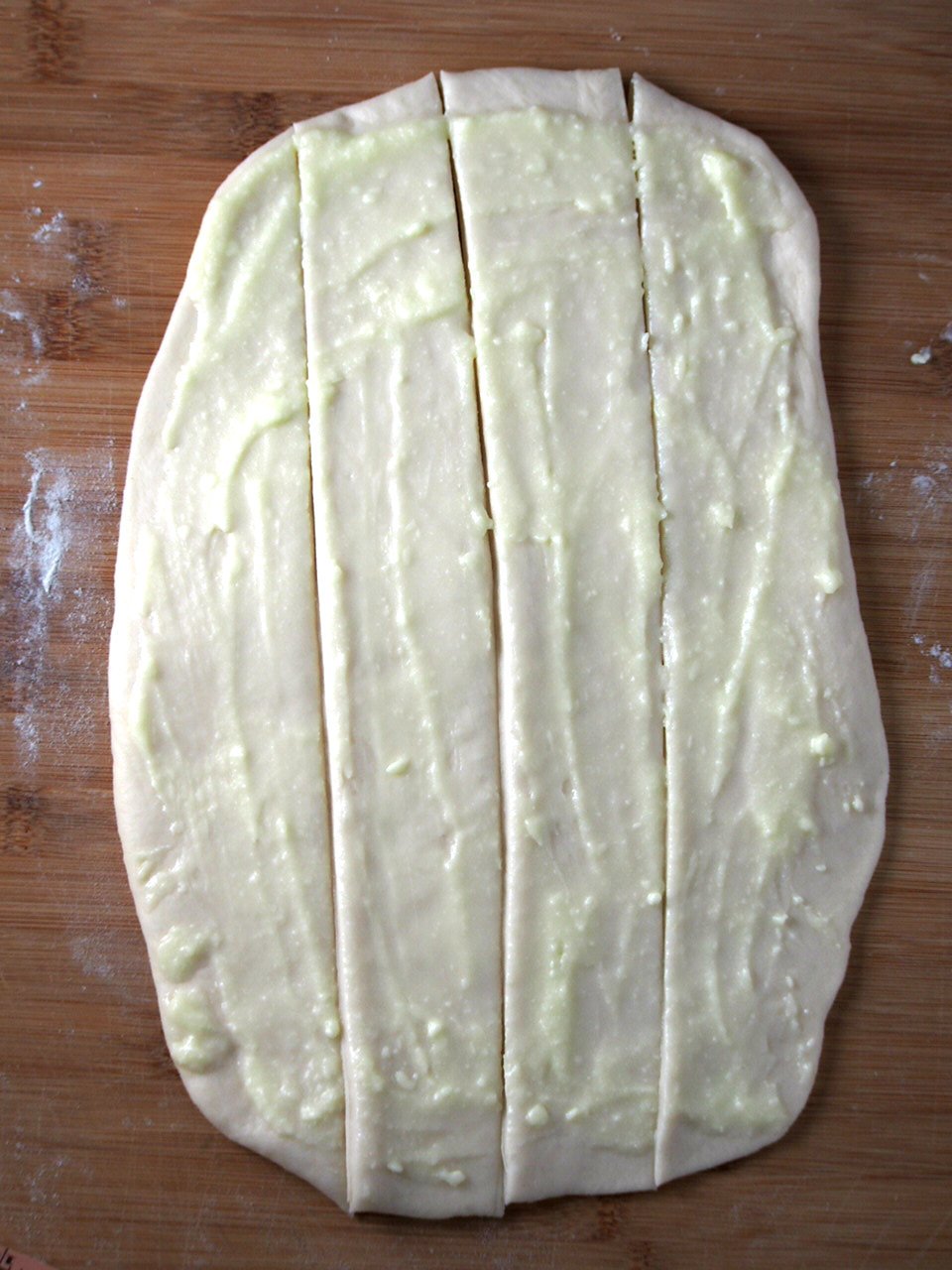 The dough is rolled into a rectangle and the condensed milk mixture is spread onto the surface of the dough. The dough is cut vertically into 4 sections.