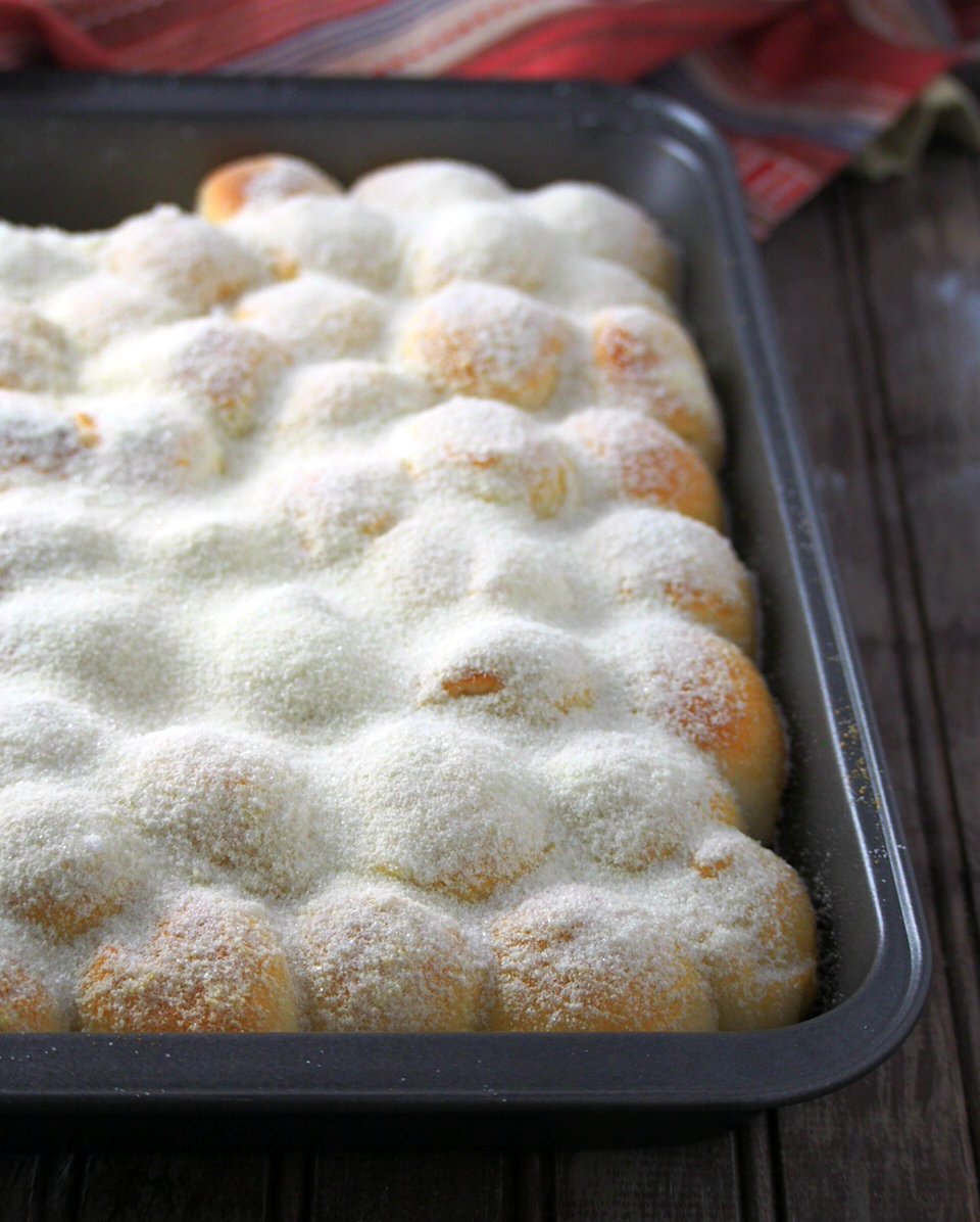 Milk and Sugar Mini Buns in a baking pan, dsted with a generous amount of milk powder and sugar.