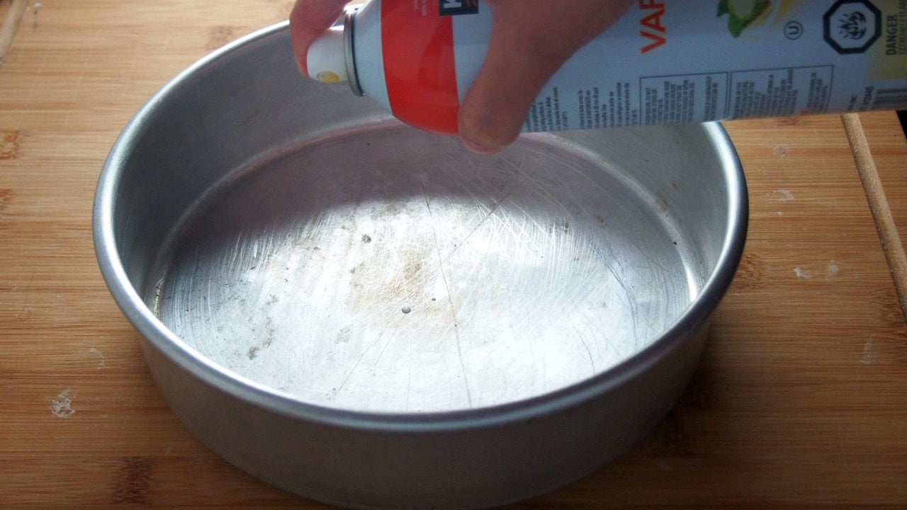 Spraying oil on the bottom of a round baking pan.