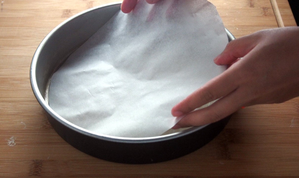 Lining the round cake pan with the cut parchment paper. 