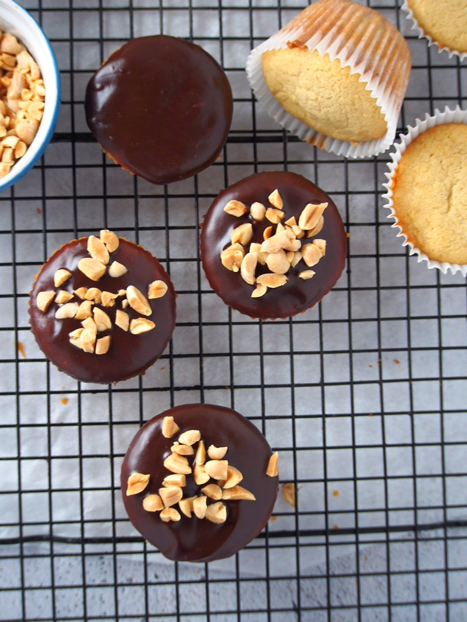 Peanut butter cupcakes on a wire rack, glazed with chocolate and top with peanuts.