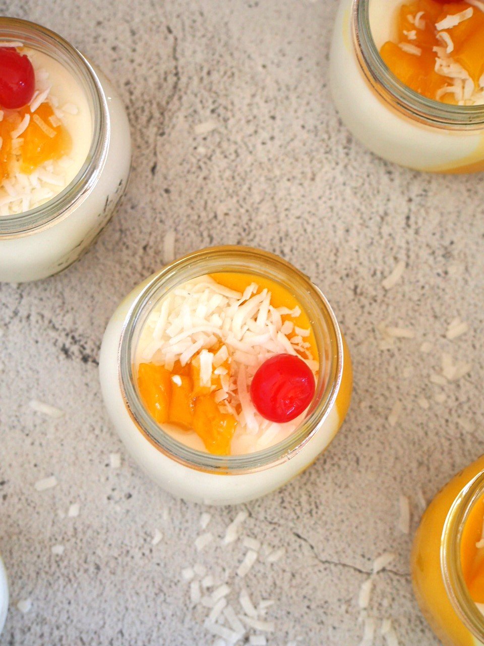 Top view shot of coconut mango panna cotta, showing the toppings of cherries , mangoes and flaked coconut.