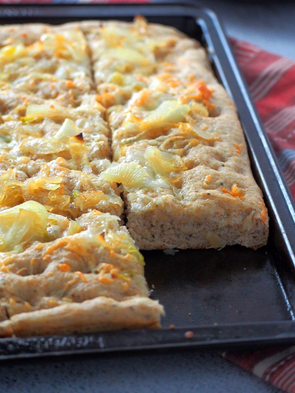 Whole wheat focaccia on a baking pan, with one slice cut out.