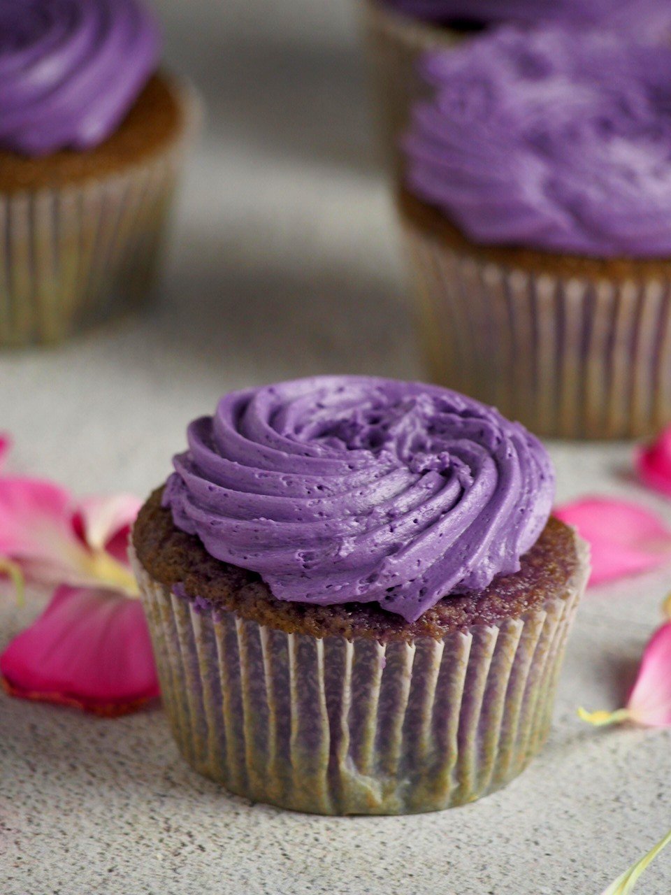 Ube cupcakes with swiss meringue buttercream surrounded by flower petals.