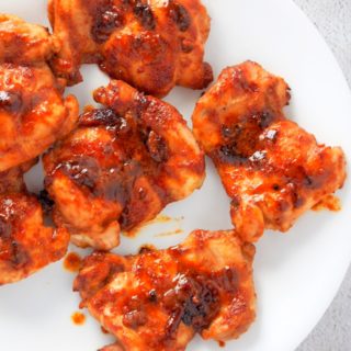 Top shot of saucy baked chicken thighs on a white plate.