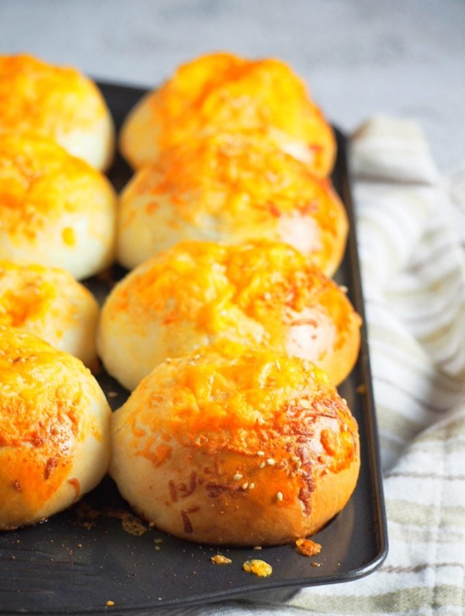 Tender crisp and cheesy tops with hints of garlic flavor, You will love these Cheddar Cheese Buns that has a bit of parmesan cheese mixed in the toppings. #cheese #cheddarbread #cheesebread