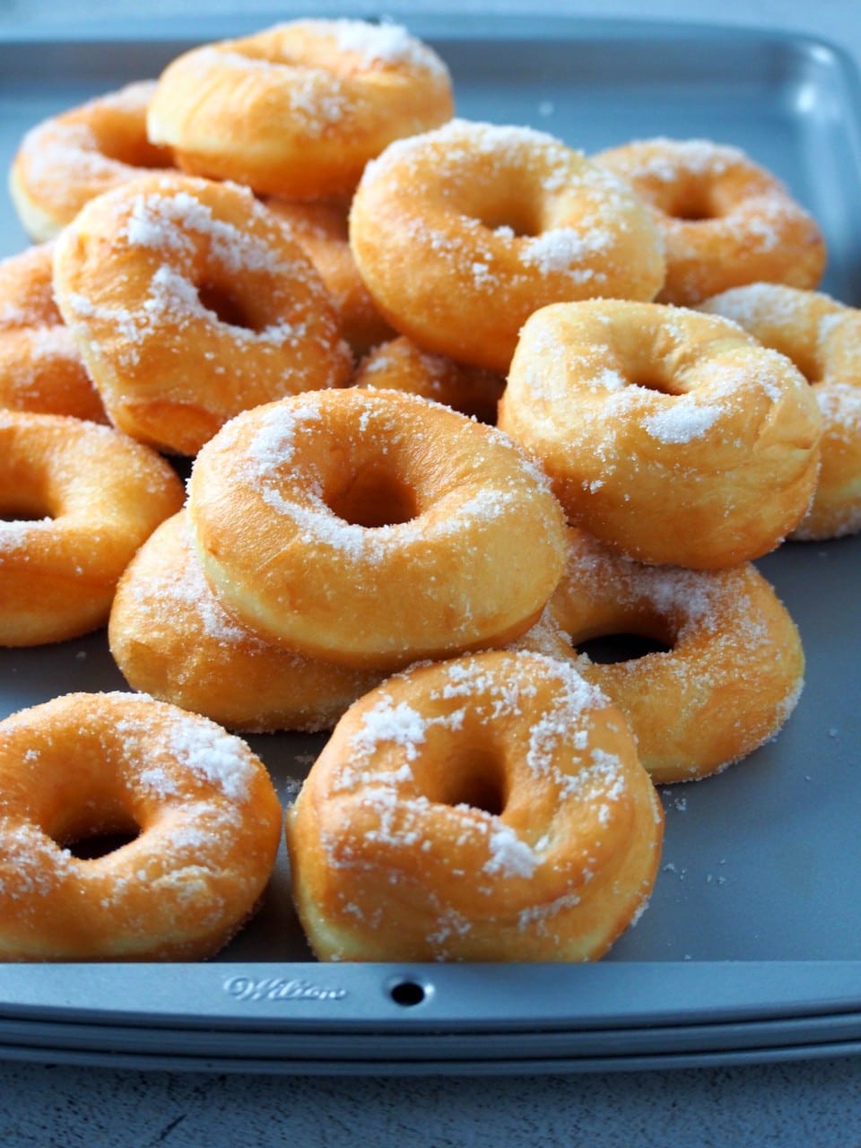 Freshly fried donuts on a baking pan.