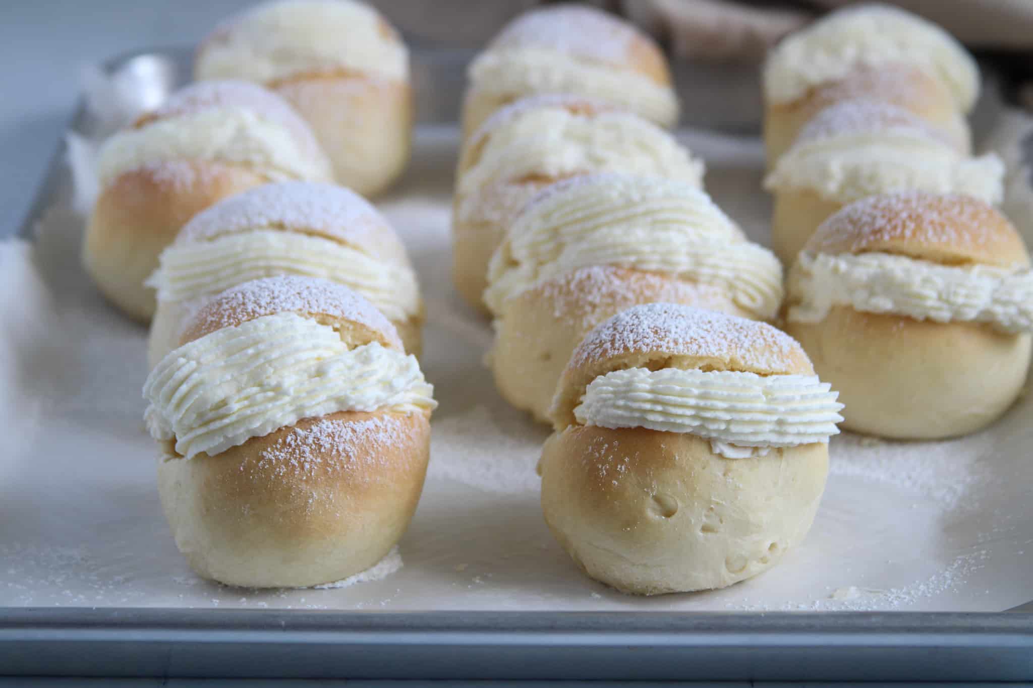 The cream buns on a baking sheet, dusted with powdered sugar.