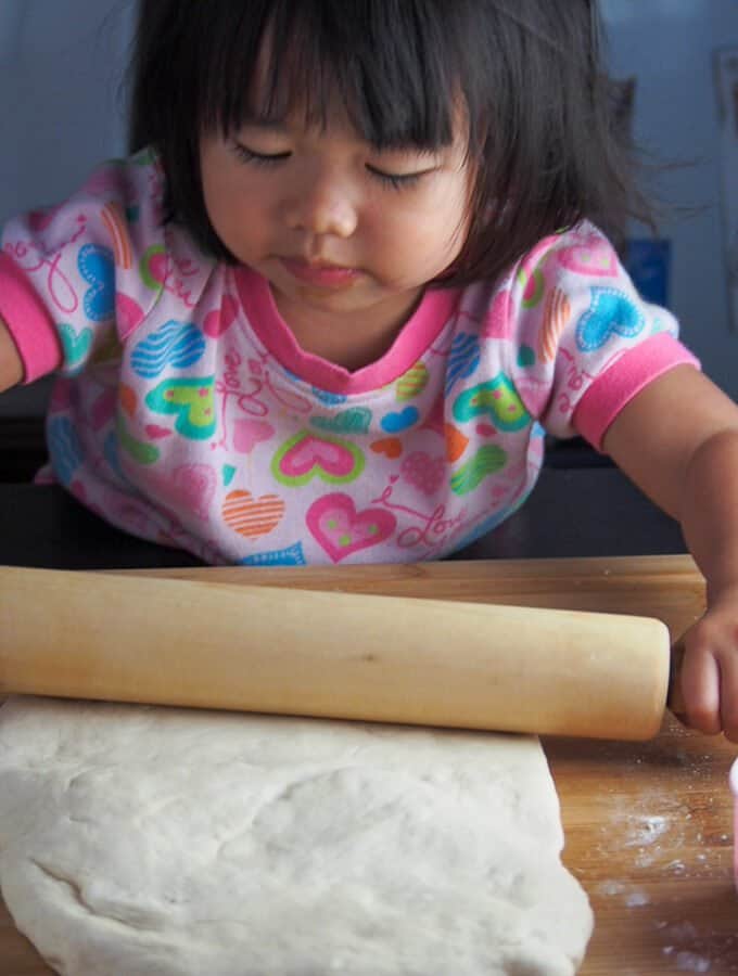 Little girl rolling dough with a rolling pin.