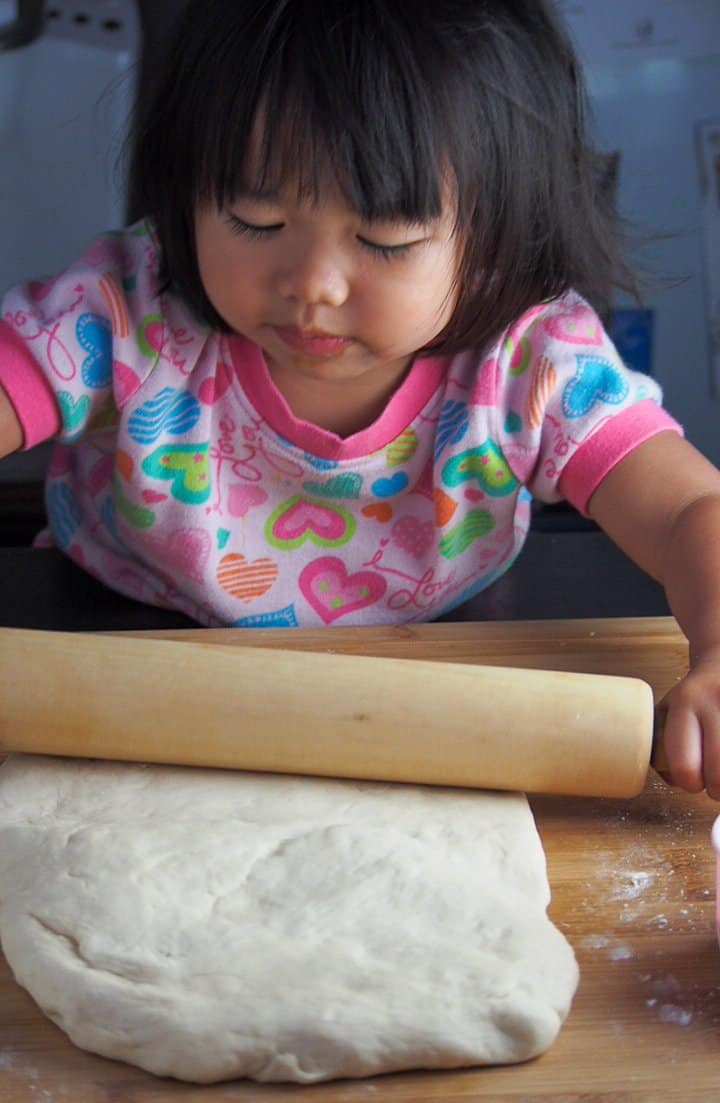 Little girl rolling dough with a rolling pin.