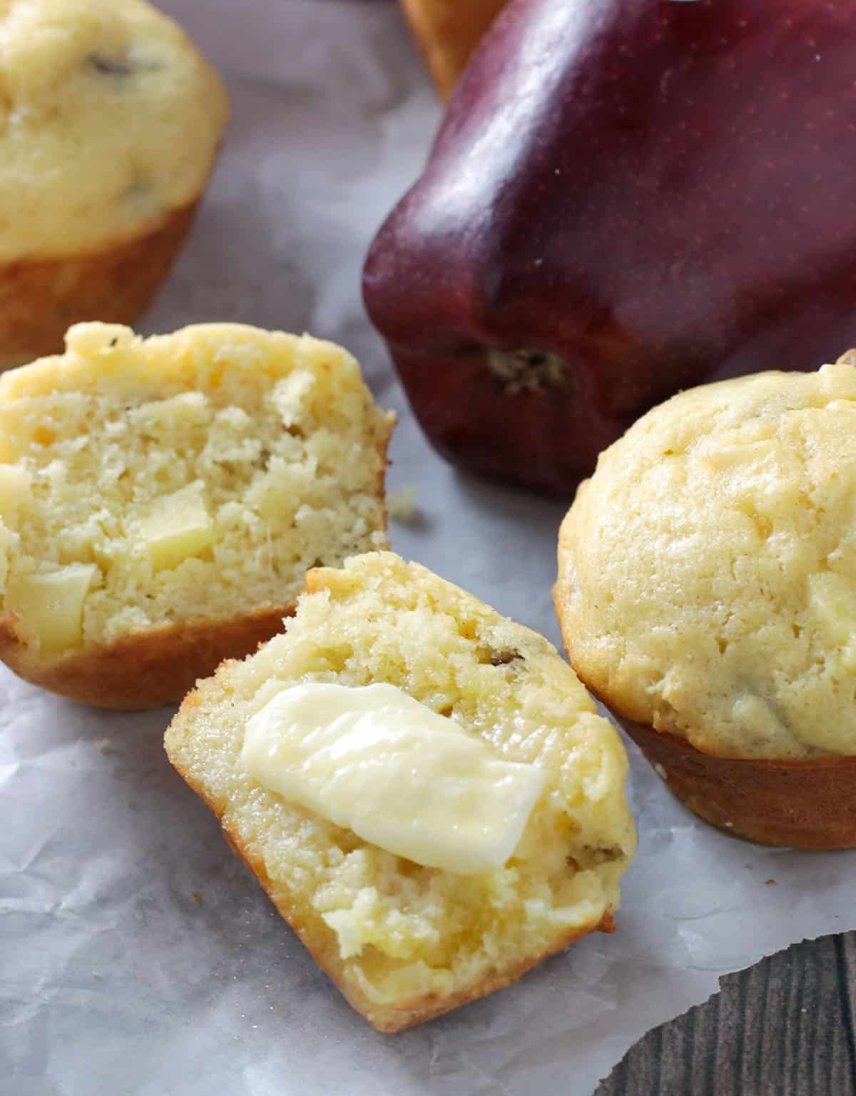 An apple cornbread muffin sliced in half and smeared with a pat  of butter.