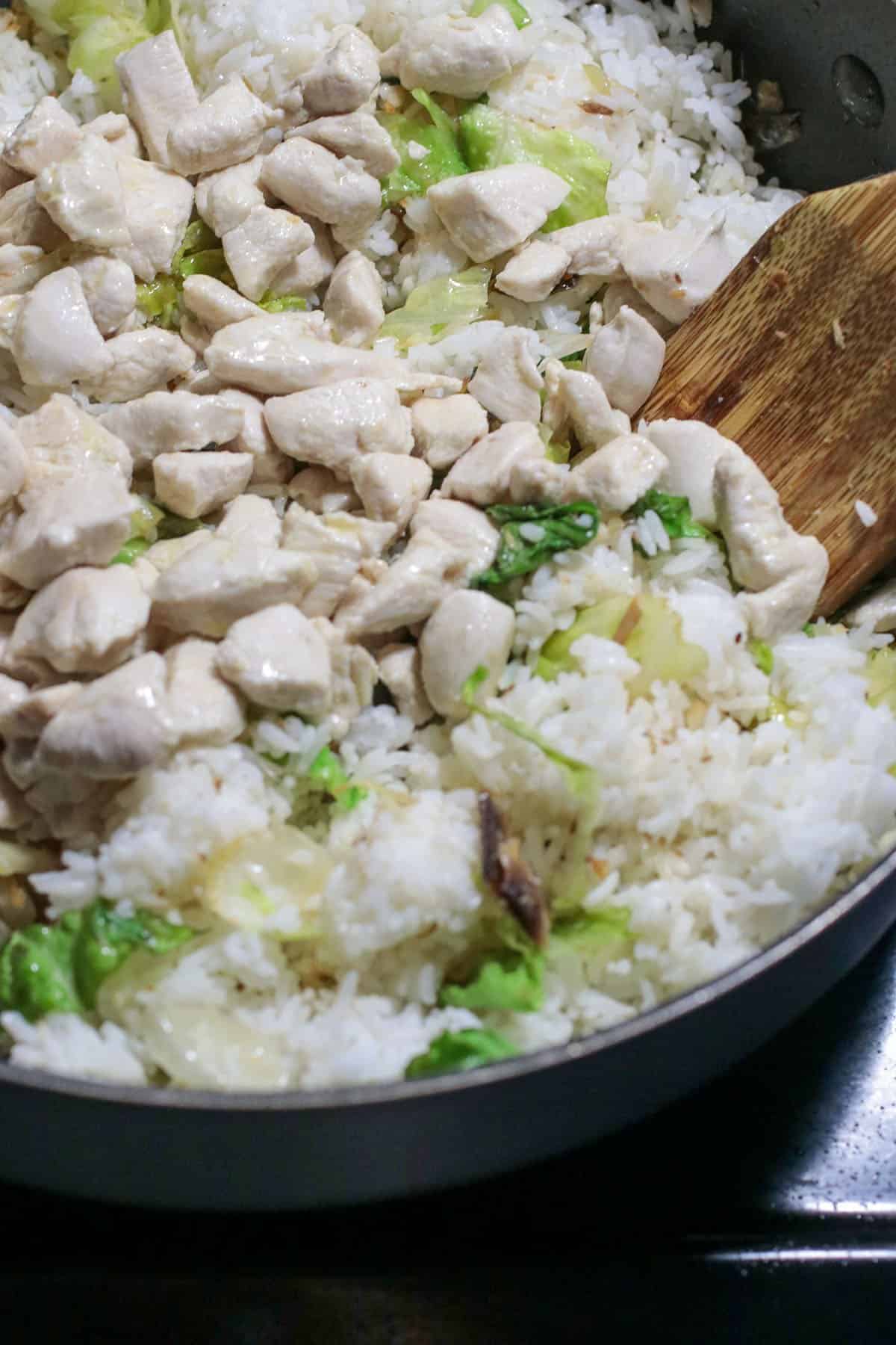 Mixing the chicken and lettuce to the rice in the pan.