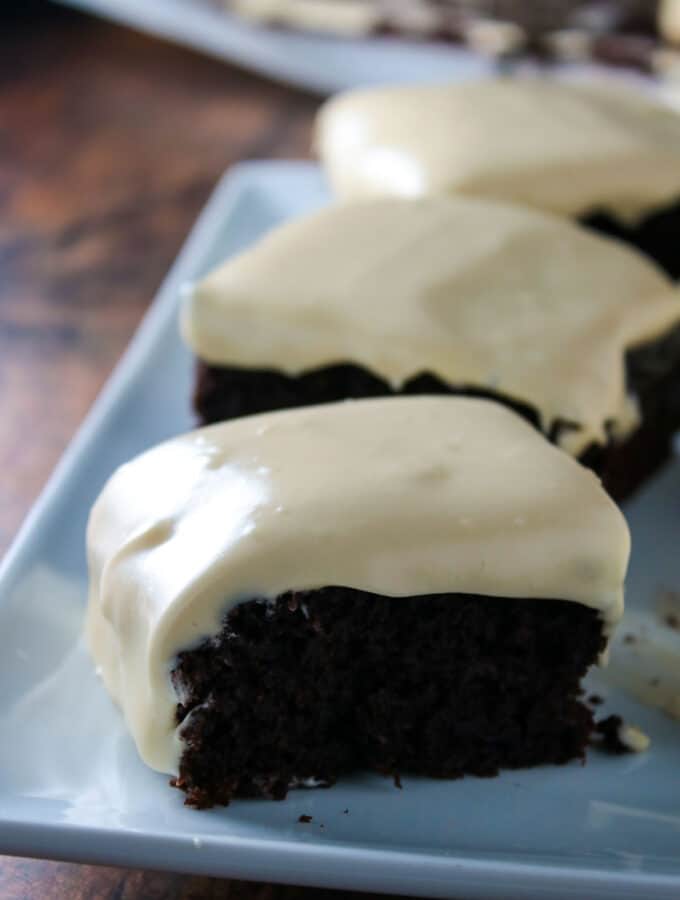 Slices of chocolate banana sheet cake with cream cheese frosting on a platter.