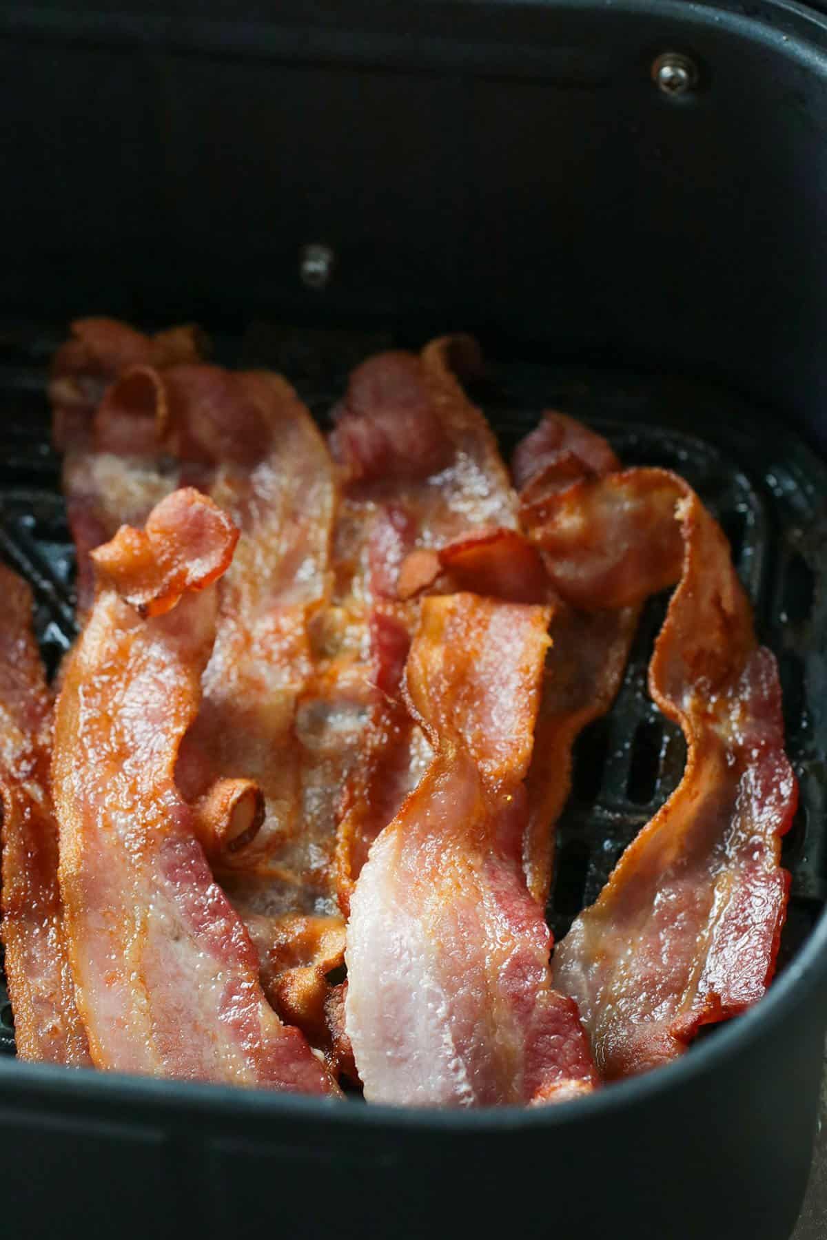Cooked bacon in air fryer basket.