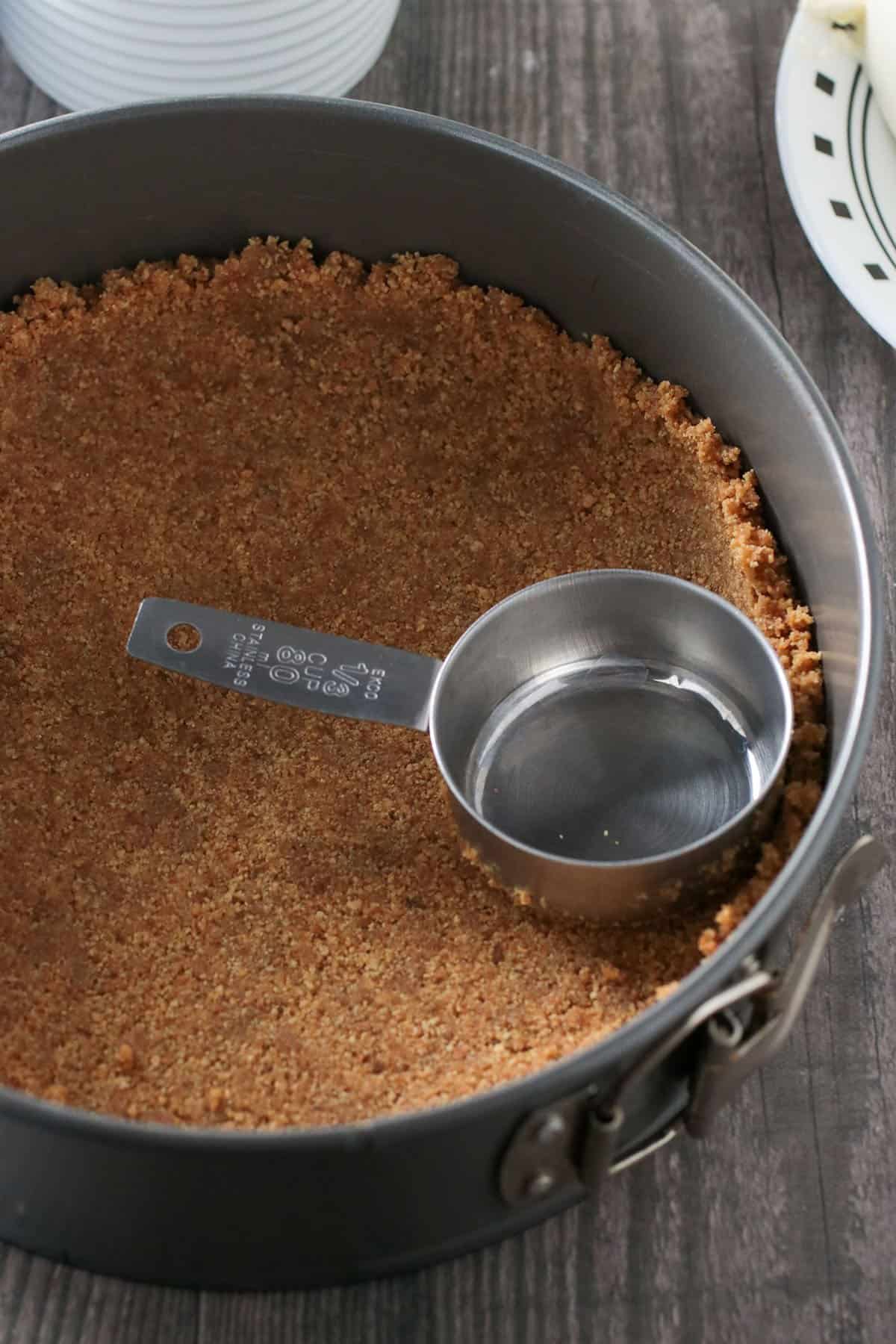 Pressing the graham crumbs mixture against a spring form pan.