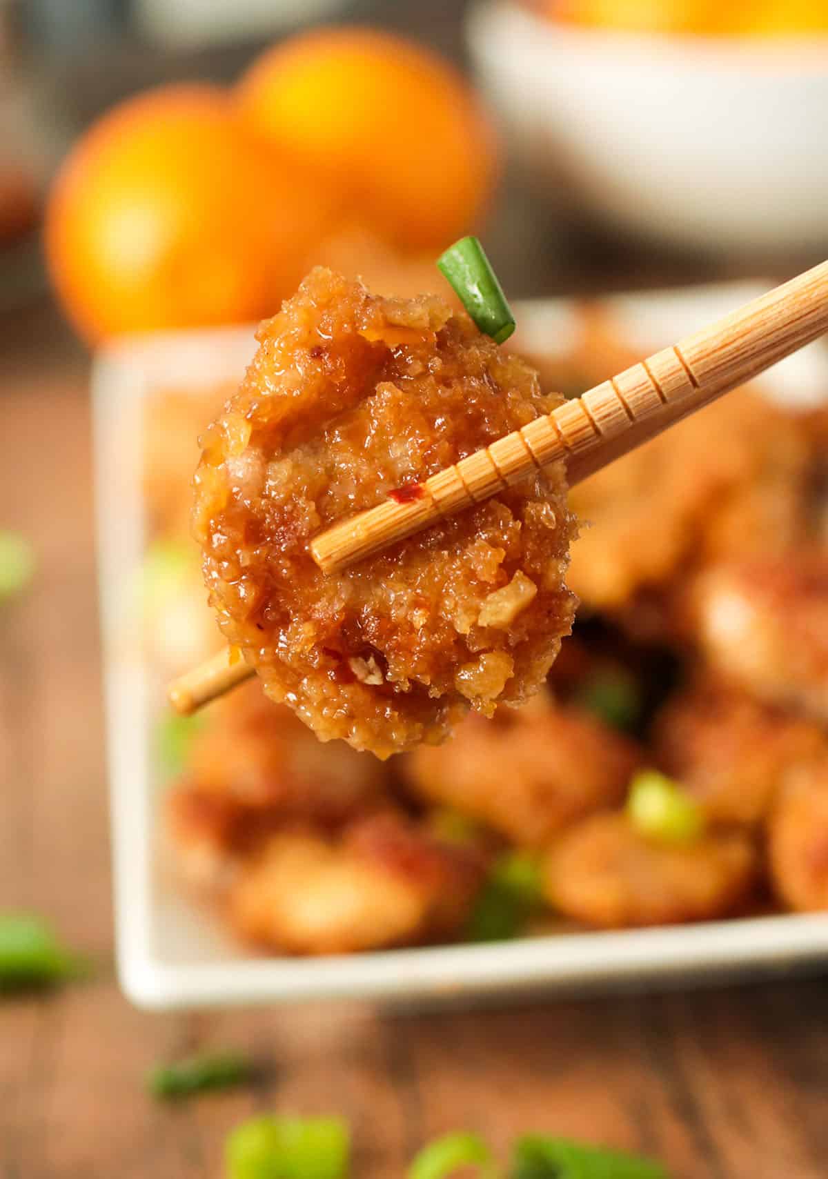 A piece of an orange chicken picked up with a chop stick.