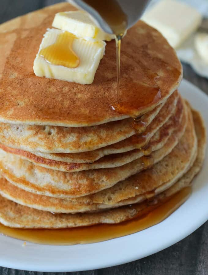 Stacked whole wheat pancakes topped with butter and maple syrup.