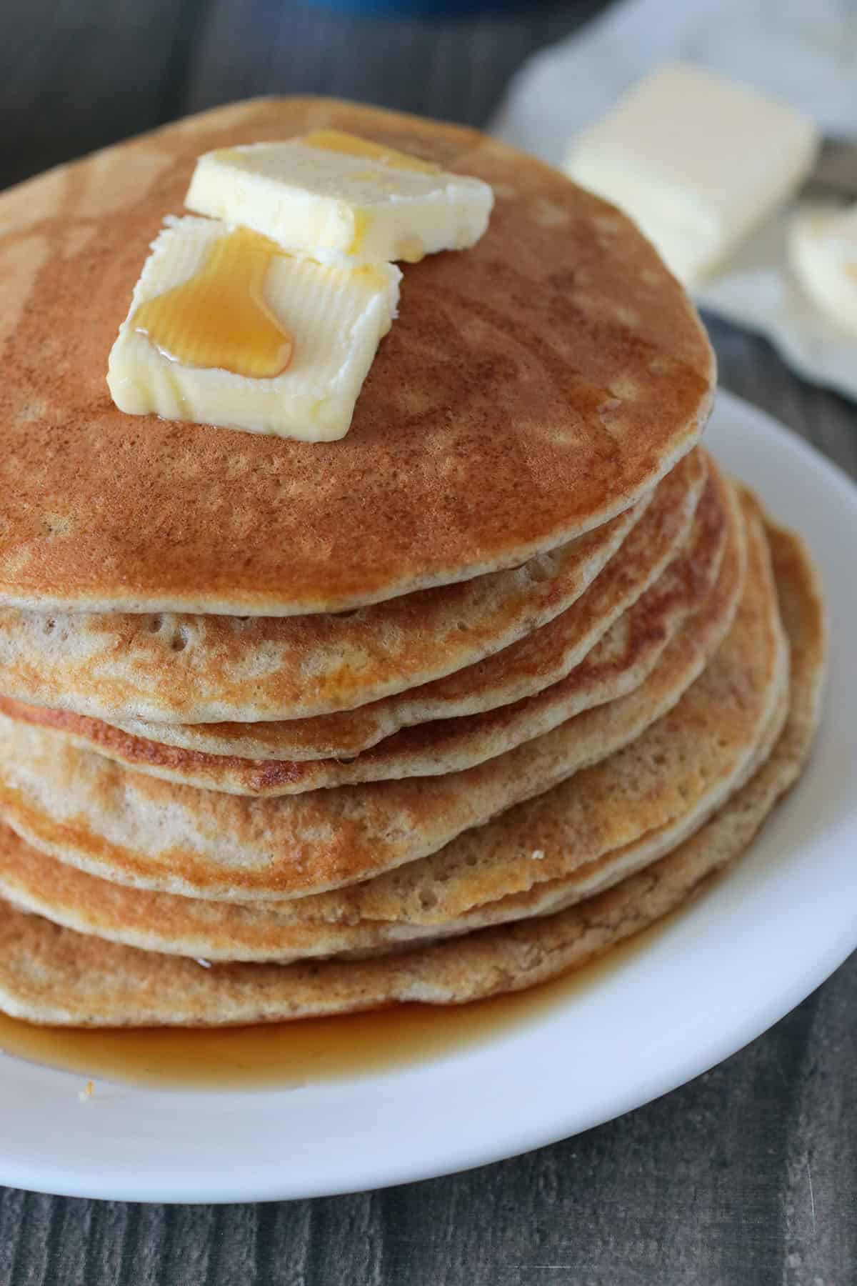 Close up of a whole wheat pancake stack topped with butter and maple syrup.