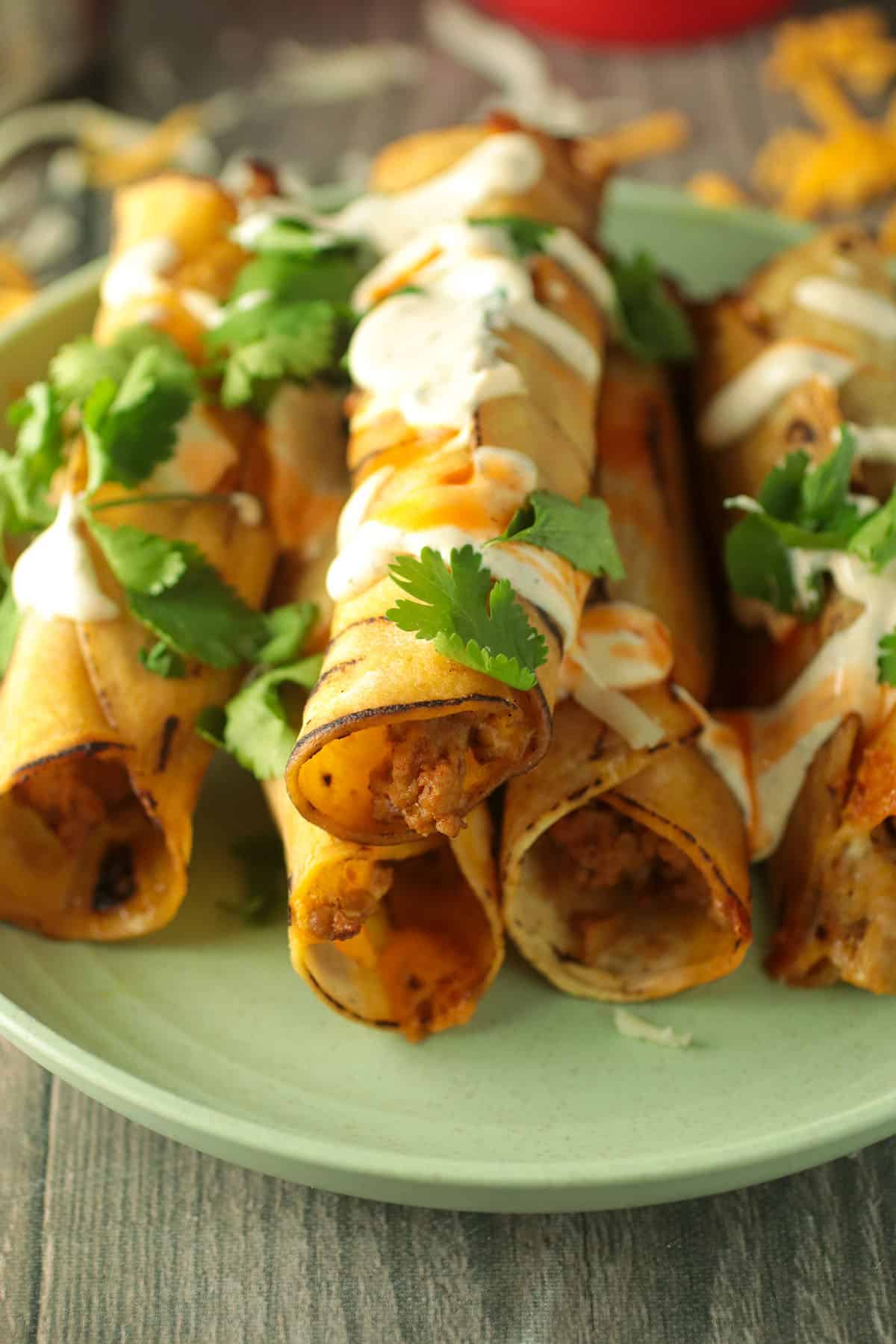 Baked turkey taquitos drizzled with hot sauce, sour cream sauce and garnished with cilantro.