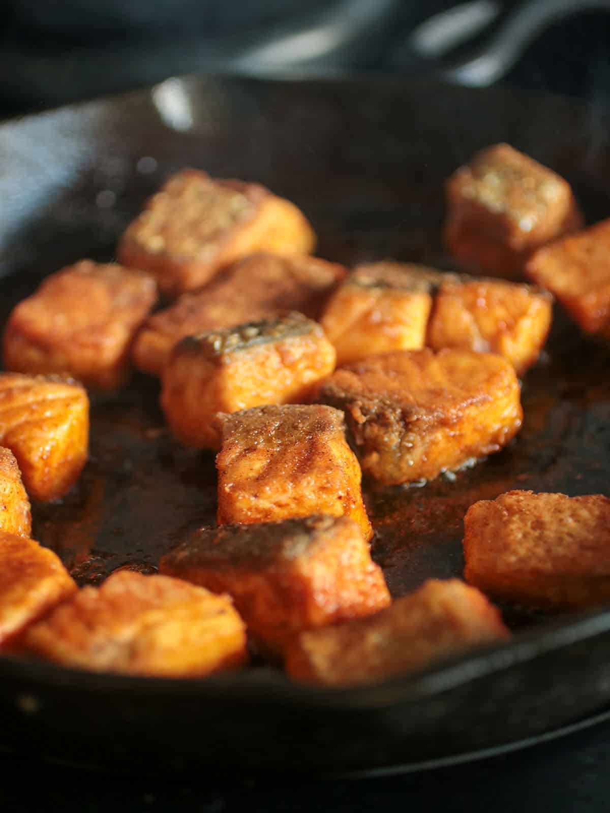 Salmon cubes frying in the skillet.