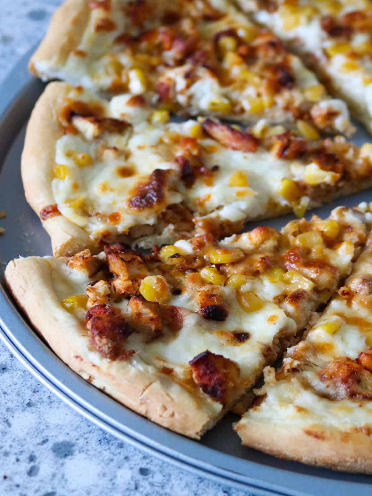 Sliced Cajun Chicken and Corn Pizza in a pan.