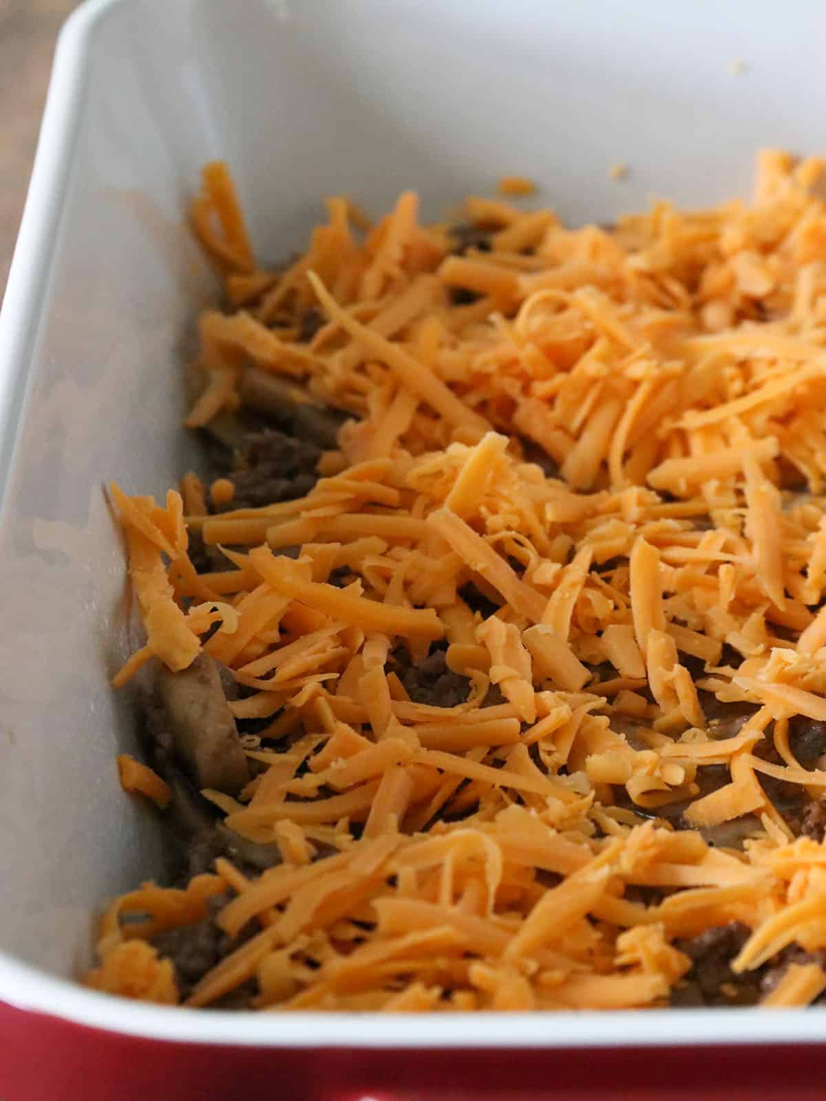 The shredded cheddar cheese sprinkled over the beef in the baking dish.