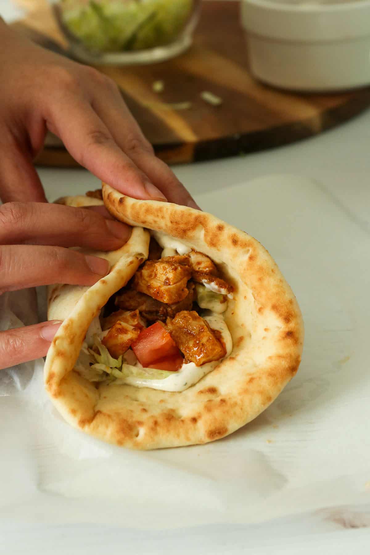 Overlapping the pita bread to enclose the shawarma filling.