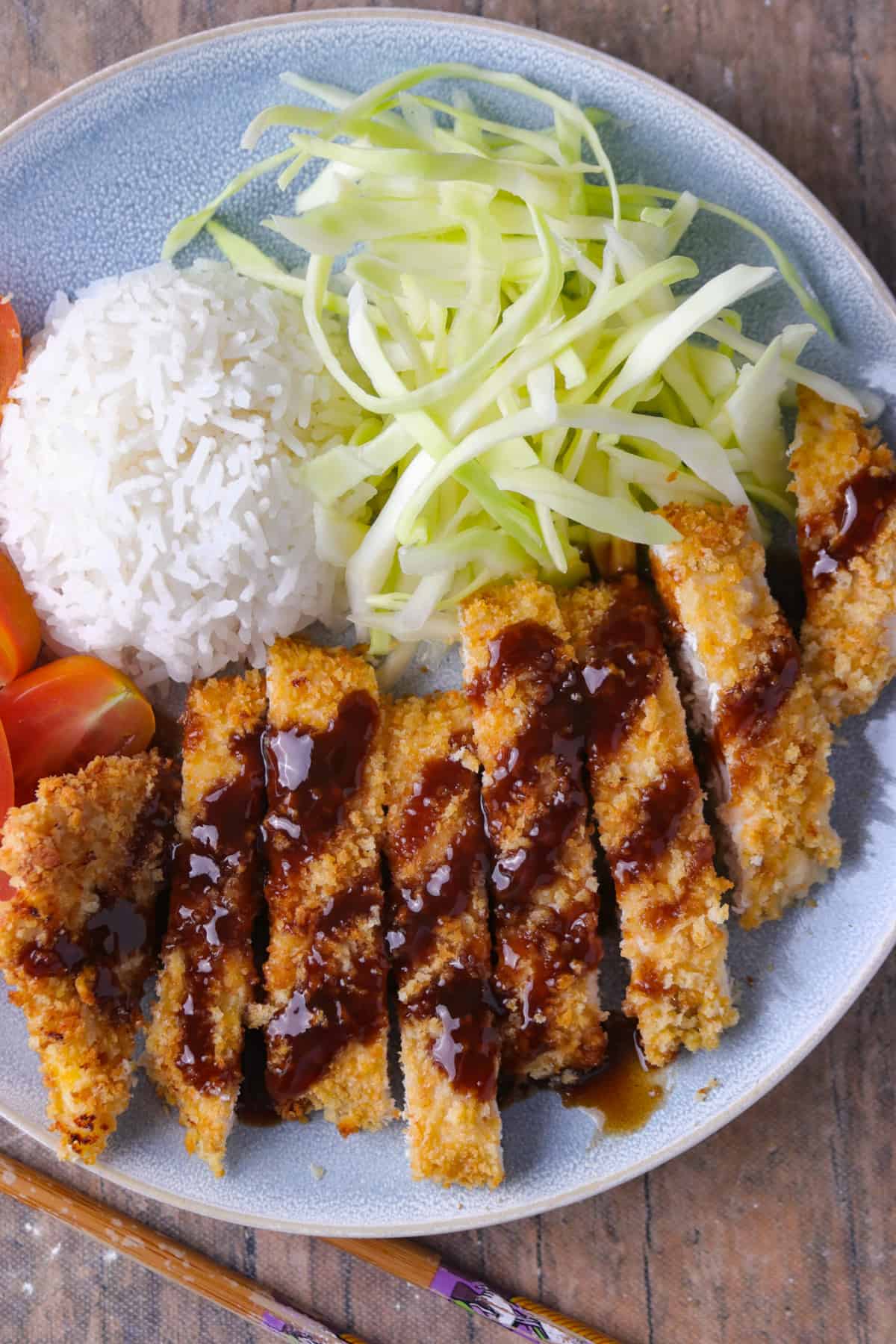 Chicken katsu served in a plate with cabbage, tomatoes and rice.